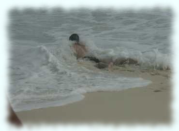 Maxl kriecht am Strand und wird von einer Welle umspült