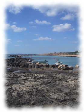 Blick vom Felsstrand zum Sandstrand mit Fischerbooten