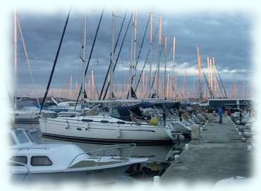 Die roten Strahlen der aufgehenden Sonne treffen auf die Masten in der Marina Šangulin