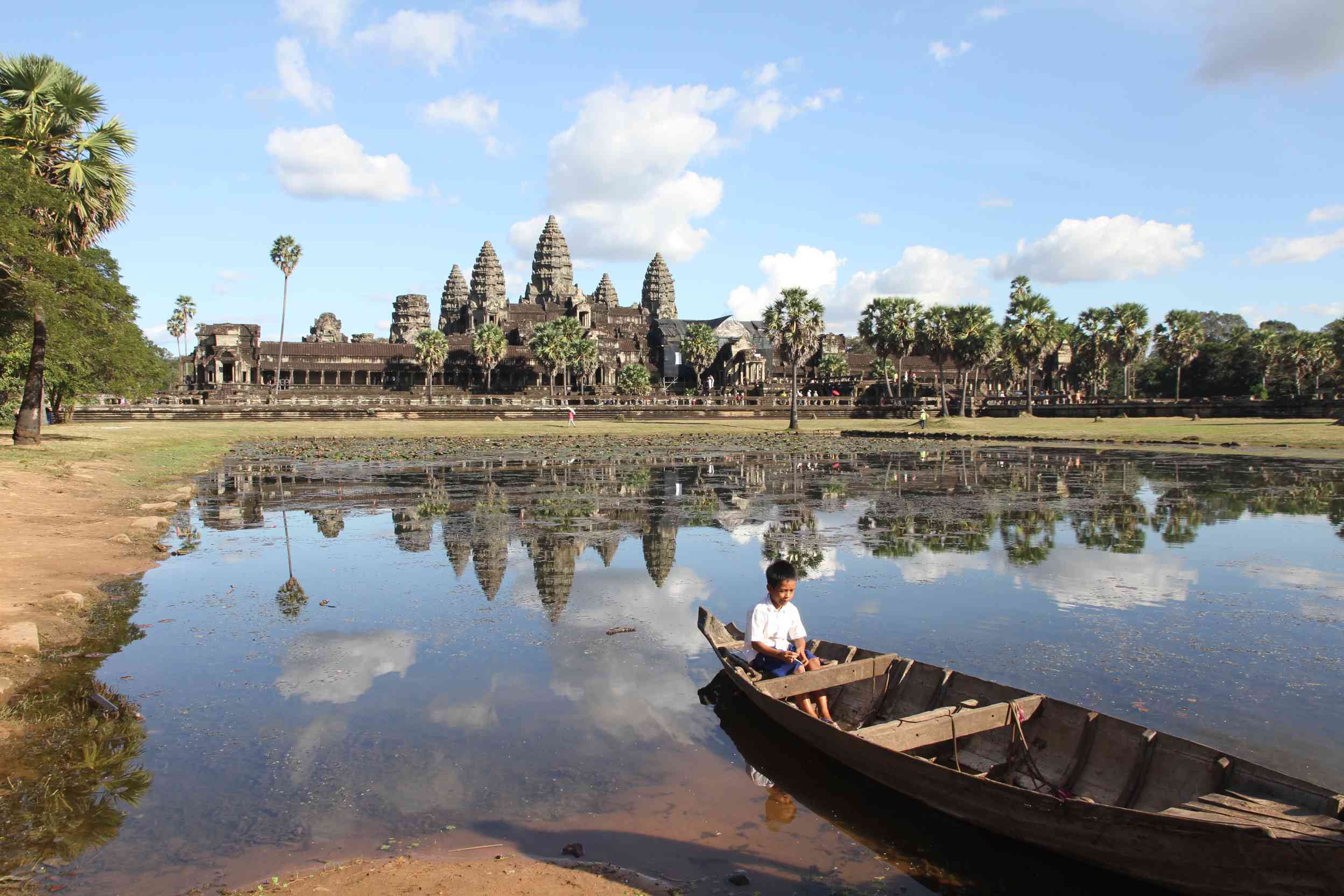 Boot mit Kind auf einem See in dem sich die Tempelanlage Angkor Wat spiegelt